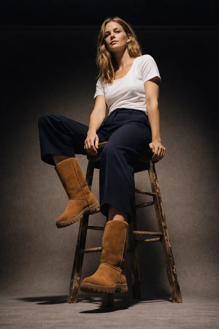 Woman wearing chestnut Classic Tall sheepskin boots in an editorial studio stool high setting